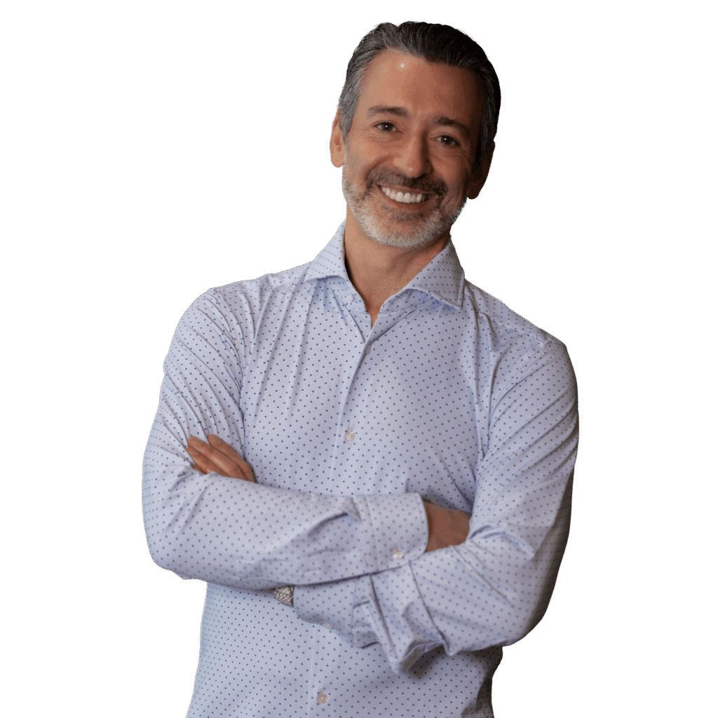 Smiling man with gray hair and beard, wearing a light blue dotted shirt, standing with arms crossed. Projects friendliness and confidence.